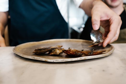 A chef's hand expertly plating seafood shells on a dish in a professional kitchen setting.