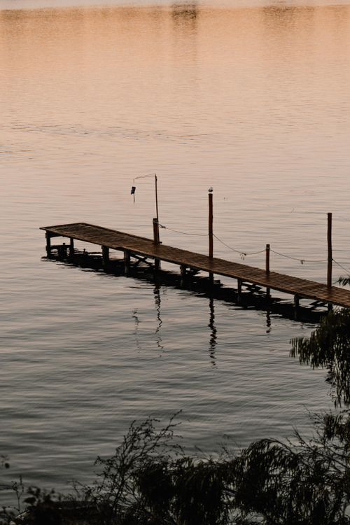 Free Wooden pier extends into calm lake at sunset, evoking serenity and natural beauty. Stock Photo