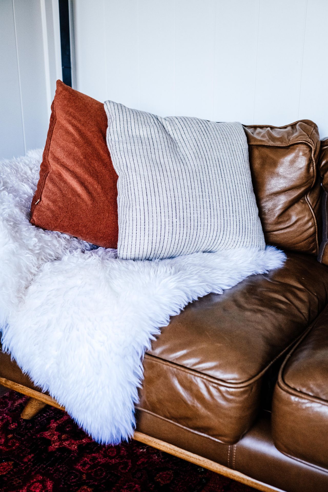 Brown leather sofa styled with a white fur throw and rust and striped pillows