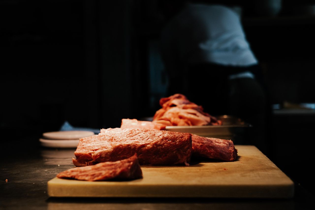 Cuts of fresh meat on a wooden board in a dimly lit kitchen