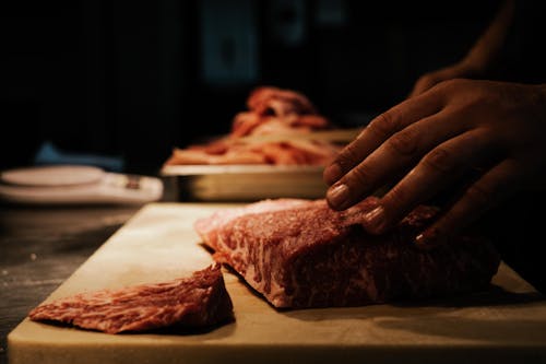Person Holding Raw Meat on Brown Wooden Table
