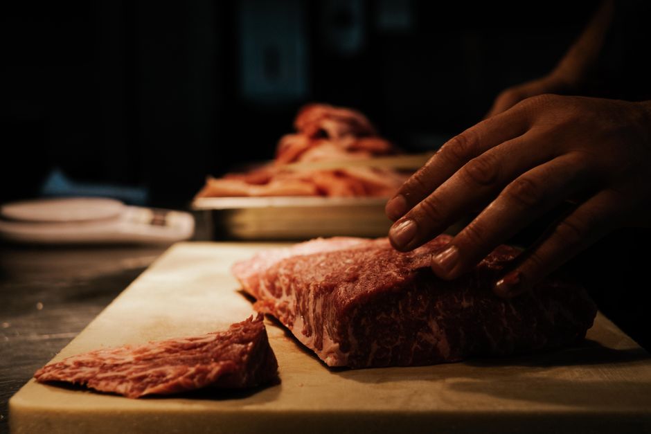 Hands of a chef preparing marbled beef on a wooden board, highlighting texture and preparation.