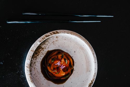 Free A close-up of a gourmet tomato dish artfully presented in a white speckled bowl with chopsticks. Stock Photo