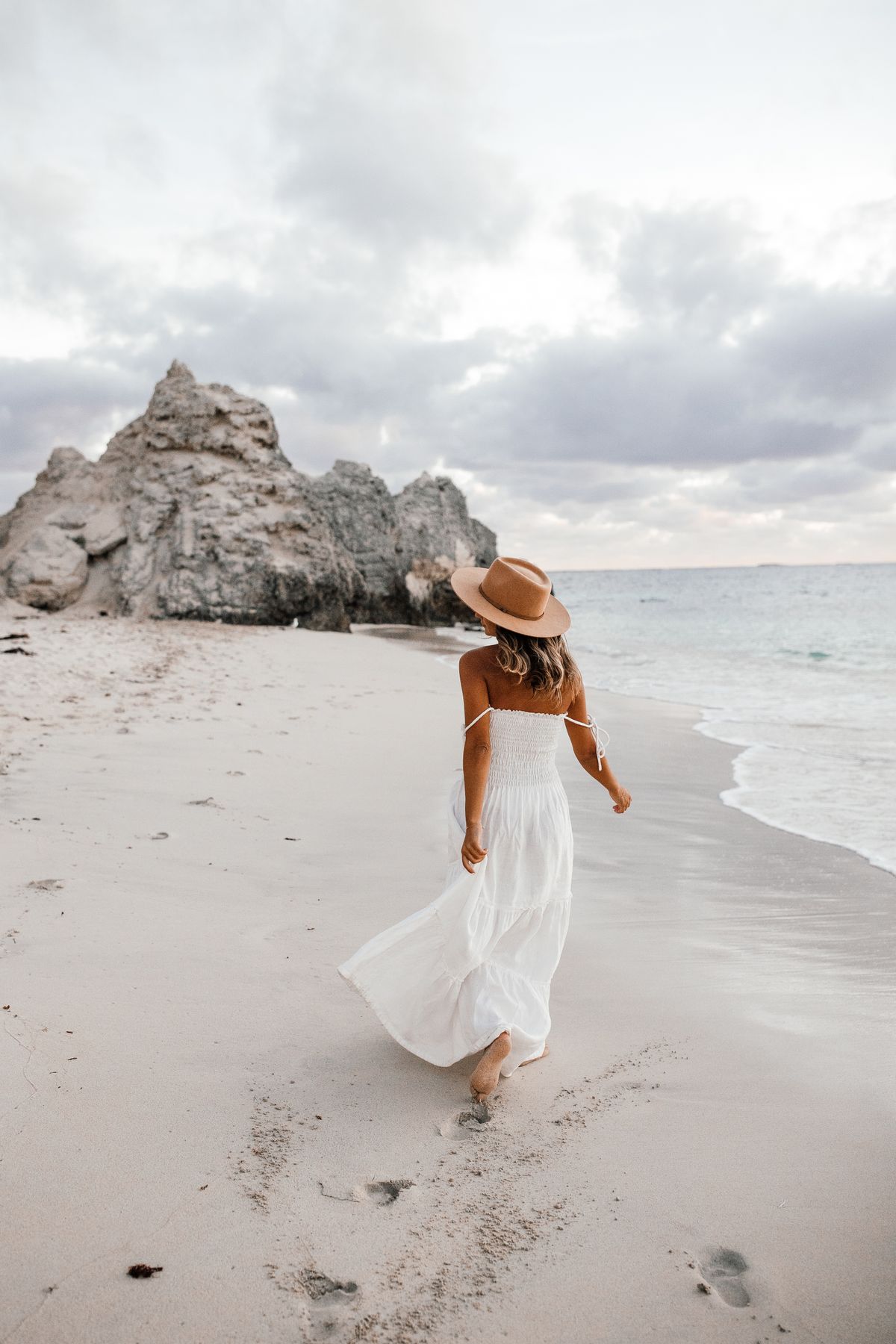 A woman in a white dress walking on the beach — the complete European summer look, at golden hour