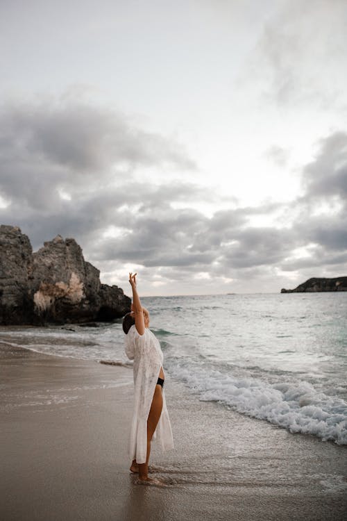 Free Woman in White Dress Raising Her Arms on Beach Stock Photo