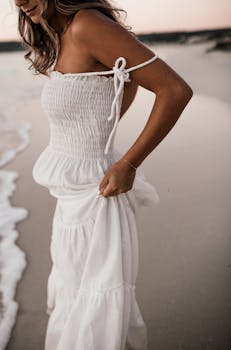 A serene beach scene featuring a woman in a flowing white dress, embodying tranquility and elegance.