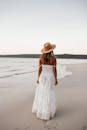 一个女人在一个白色的衣服和帽子走在一个空的海滩在日落