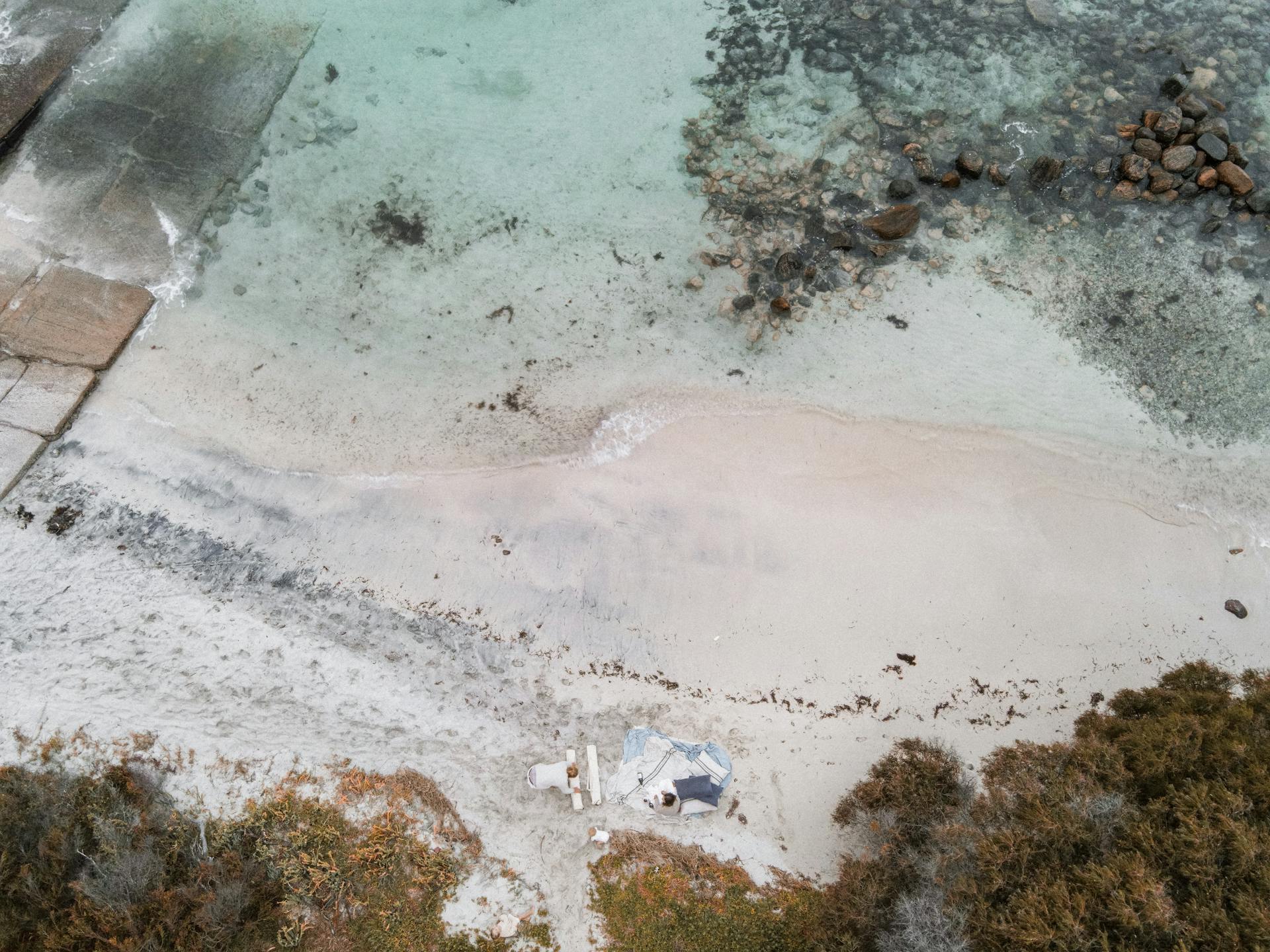 A serene aerial beach view with a tent, rocks, and clear waters, ideal for relaxation.