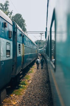 People walking between two blue trains at a railway station, showing public transportation hustle.