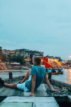 A man sitting on a boat overlooking a vibrant cityscape during the evening.