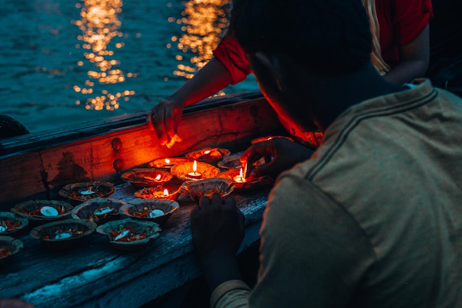 People lighting candles on a boat during an evening water ceremony, creating reflections on the water surface.
