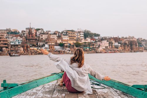 Free Woman sitting on a boat with arms raised, overlooking the ghats of Varanasi, India. Stock Photo
