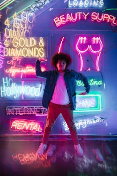 A stylish young man poses confidently surrounded by vibrant neon signs.