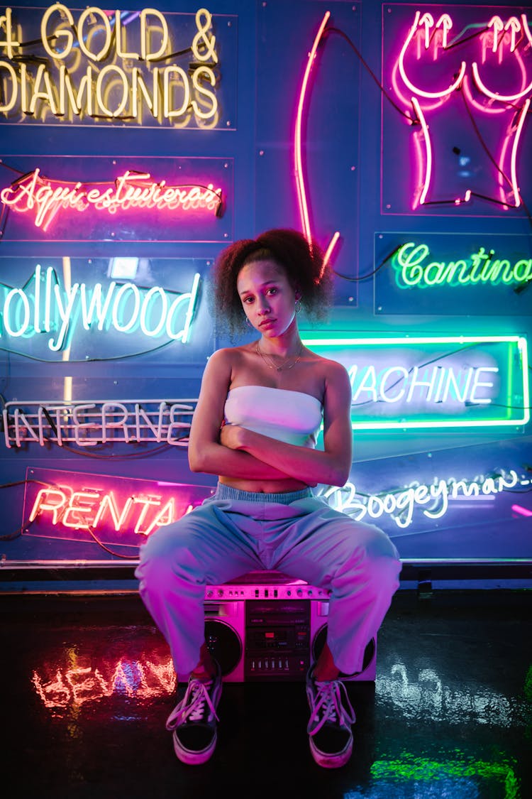 A Woman In White Tube Sitting On A Stereo While Looking At The Camera