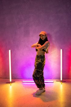 Young woman in a stylish dance pose surrounded by vibrant neon lights.