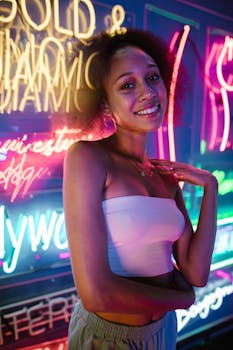 Smiling young woman poses against colorful neon signs in a lively scene.