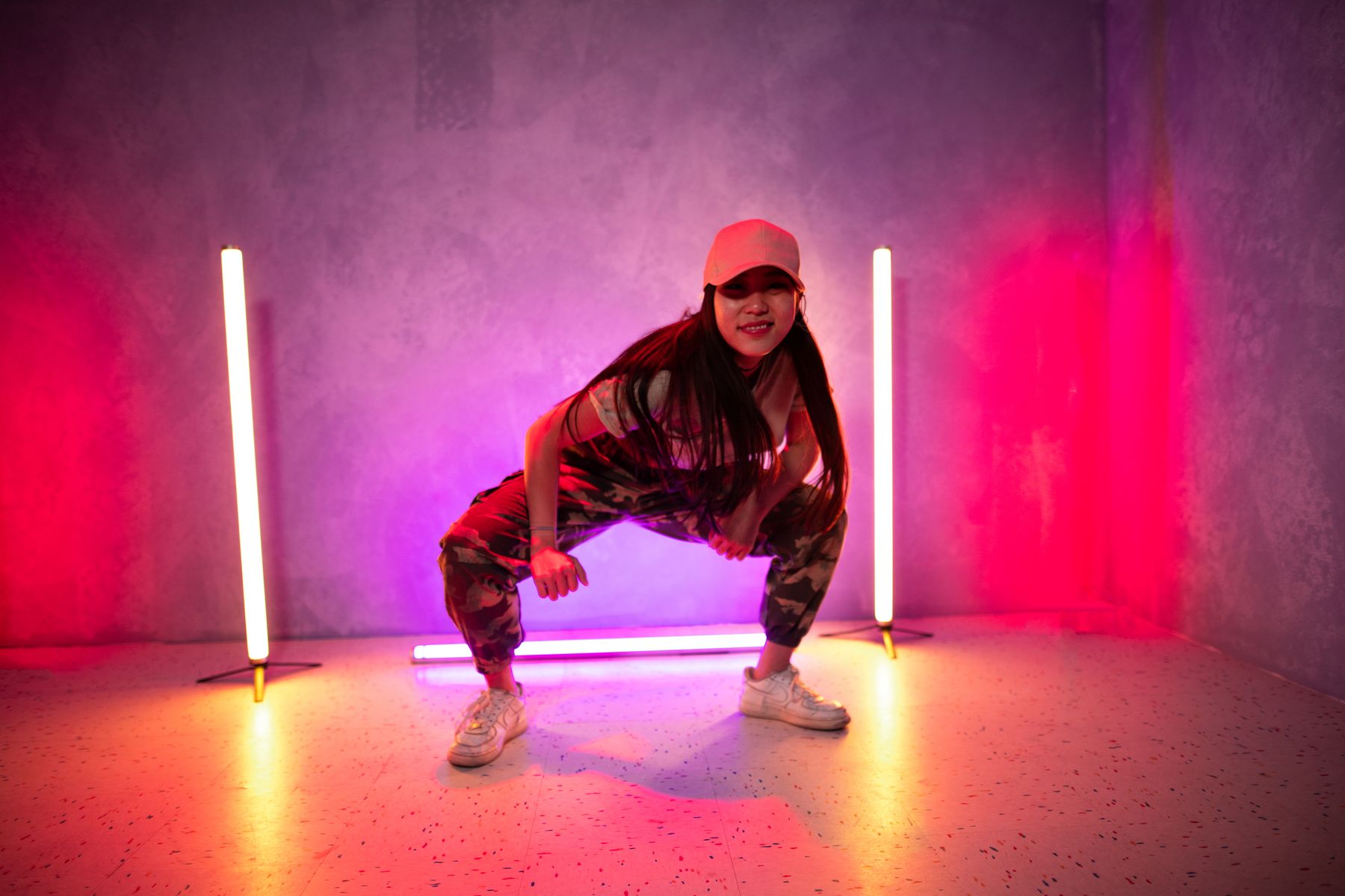 Bailarina de hip hop en cuclillas entre dos tubos de luz de neón
