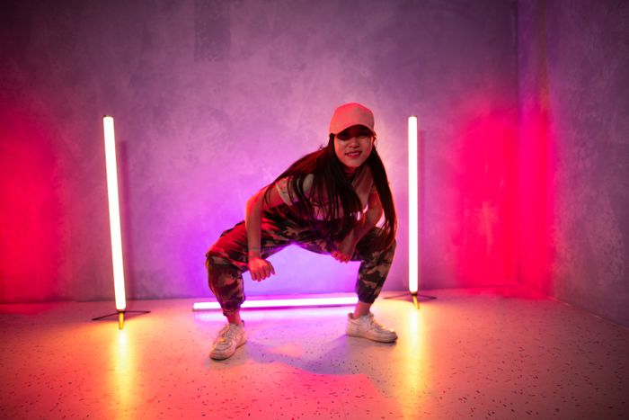 Bailarina de hip hop en cuclillas entre dos tubos de luz de neón