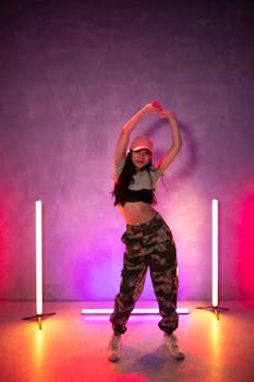 Trendy woman in crop top dancing in camo pants under vibrant neon lights.