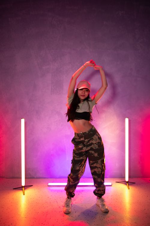 Free Trendy woman in crop top dancing in camo pants under vibrant neon lights. Stock Photo