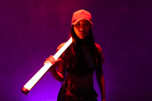 Artistic portrait of a young woman in street style holding a neon light tube against a dark background.