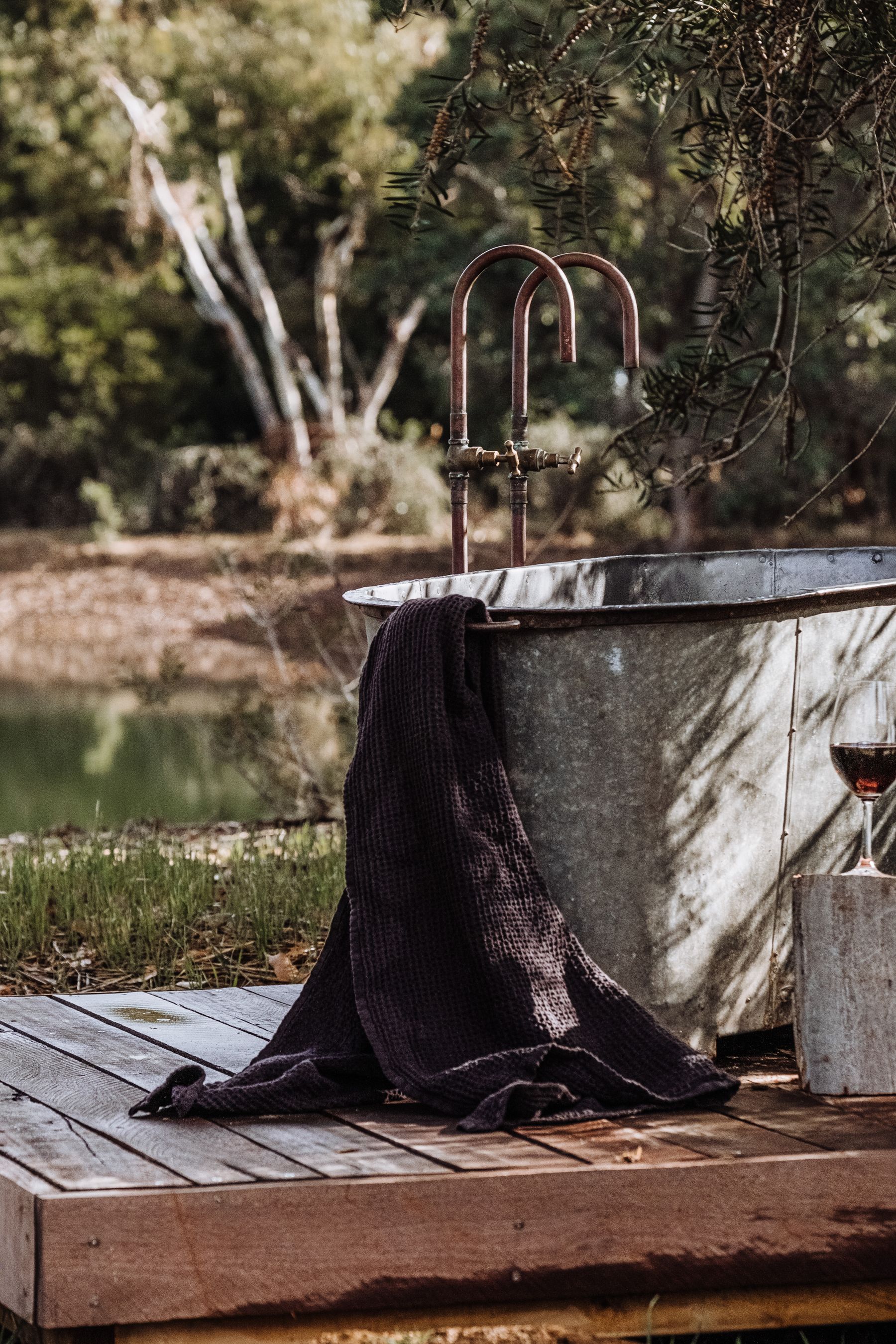 Outdoor metal bathtub on a timber platform beside a natural landscape