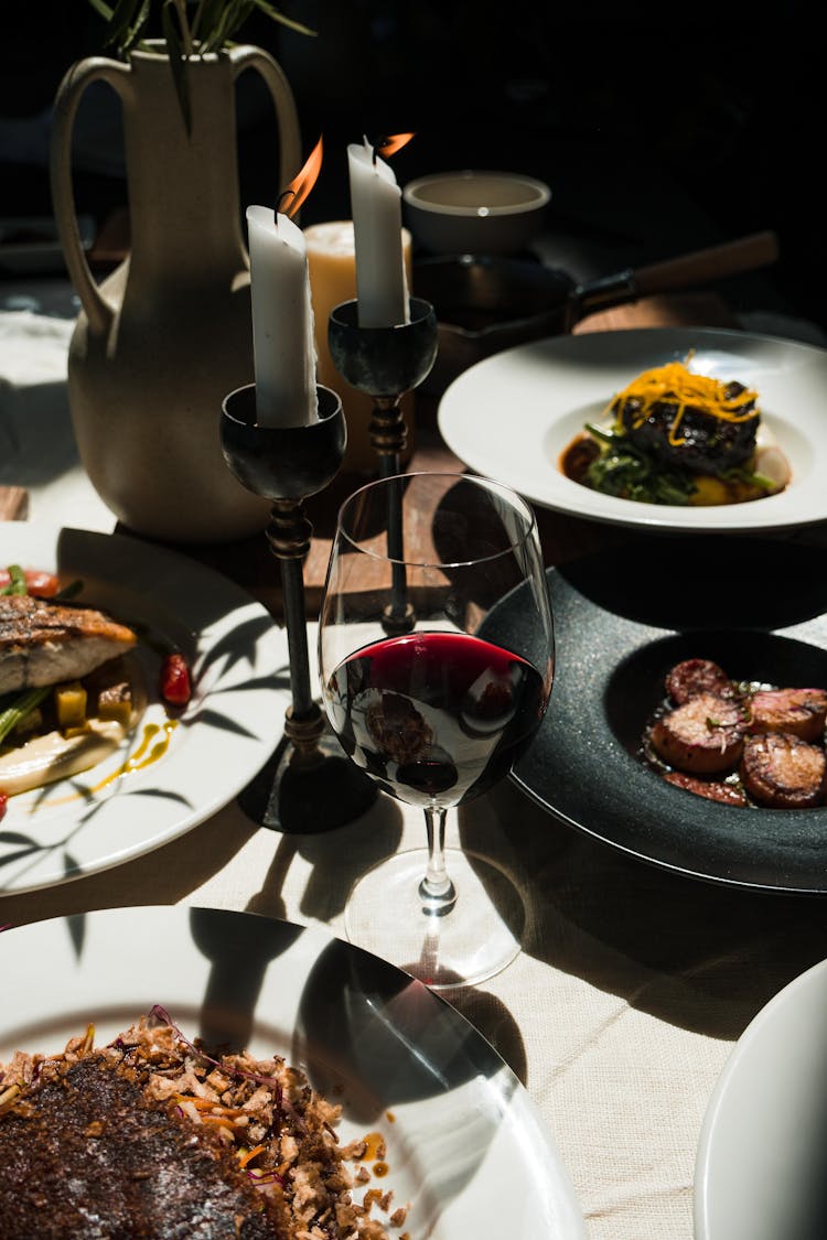 Cooked Food On White Ceramic Plates And Glass Of Red Wine On Table