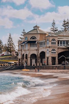 Beachfront view of historic building at Cottesloe Beach, WA. Waves washing ashore under blue sky.