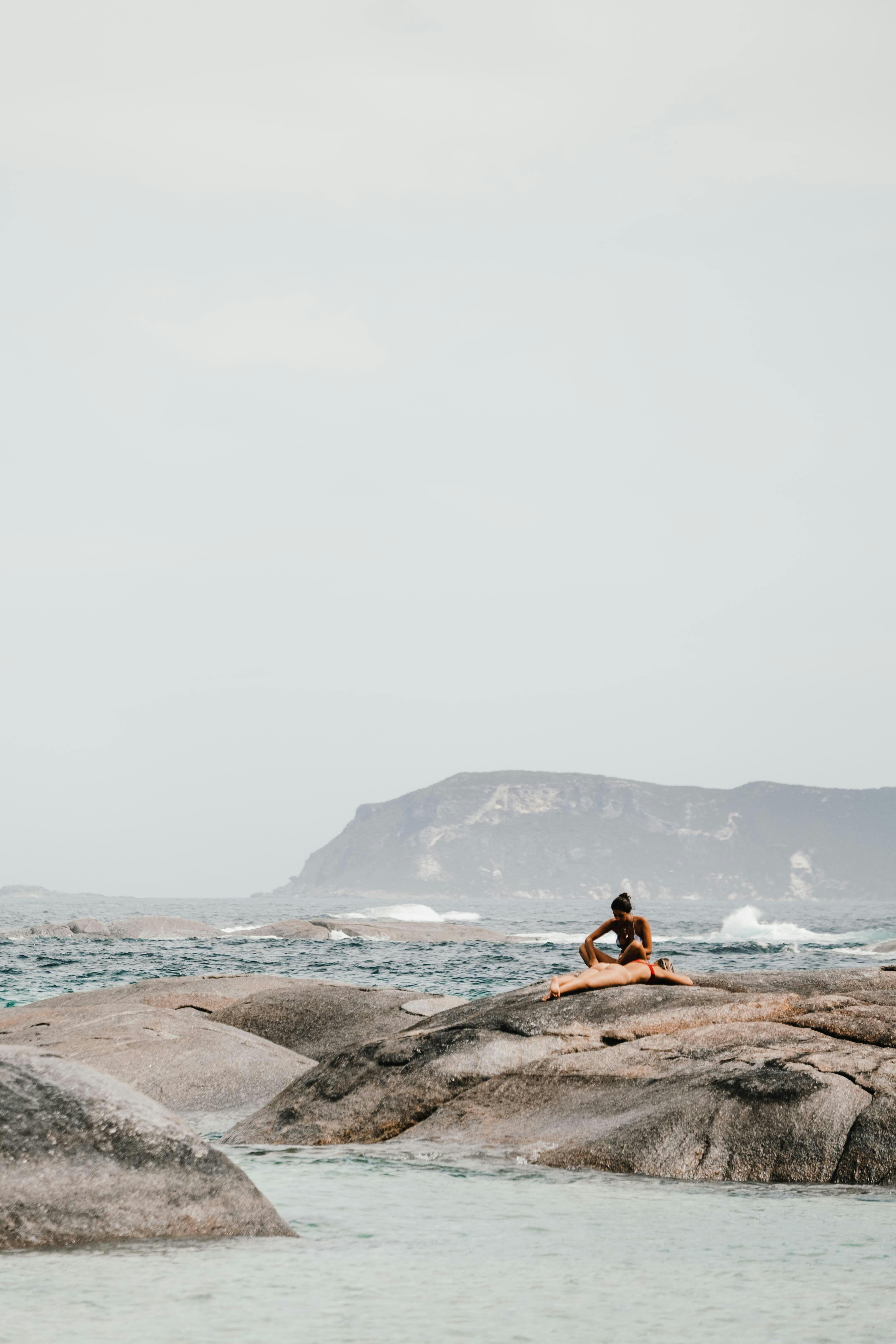 人们在海边的岩石上晒日光浴，可以看到远处的山景