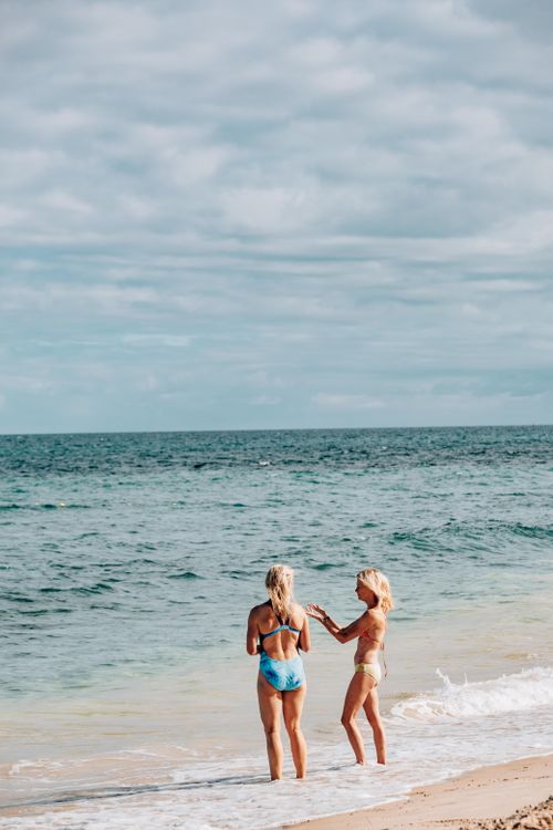 Free Two women in bikinis enjoy a sunny day at the beach with a serene ocean view. Stock Photo