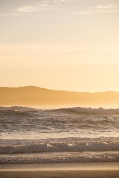 Serene view of ocean waves at sunrise with silhouetted hills in the background.