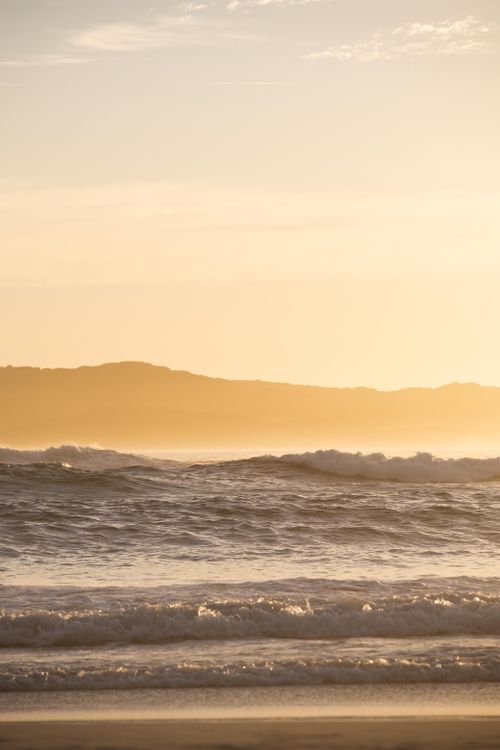 Free Serene view of ocean waves at sunrise with silhouetted hills in the background. Stock Photo