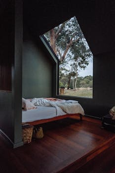 Cozy bedroom interior with a large window showcasing a natural view, emphasizing minimalist design.