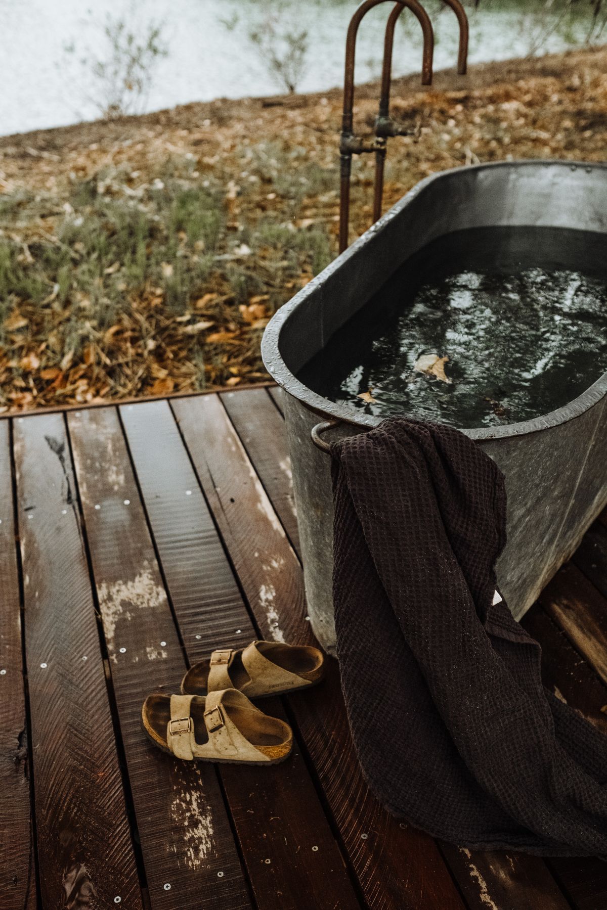 A rustic open-air wooden bath on a deck with a towel and sandals, evoking a quiet Kinosaki ryokan