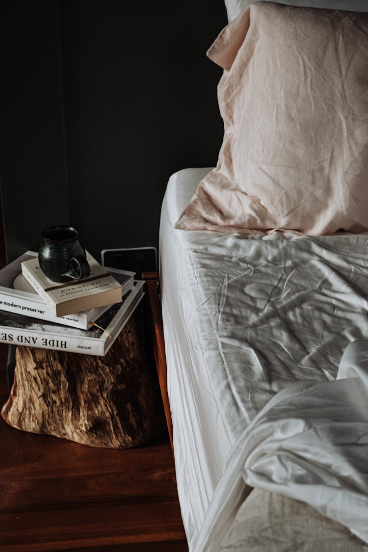 Stack Of Books Next To A Bed 