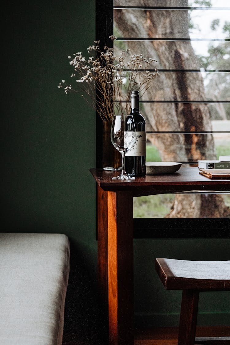 Wine Bottle, Glass And Plant On Table Near Window And Bed