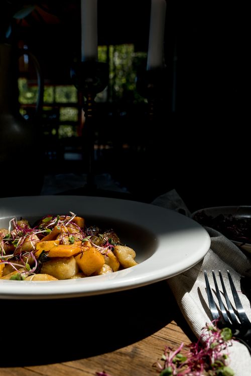 Free Delicious gnocchi dish garnished with fresh herbs and vegetables under warm lighting. Stock Photo