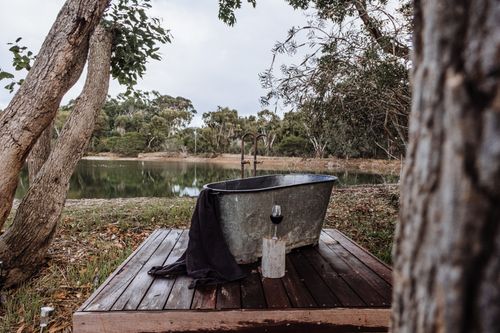 Free Relaxing rustic outdoor bathtub on a wooden terrace by a serene lakeside view. Stock Photo