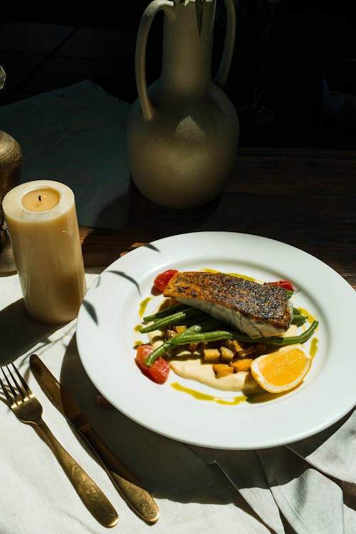Photo of a Dish with Fish Beside a White Candle