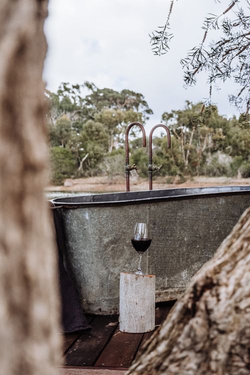 Free A serene outdoor bathtub scene featuring a glass of red wine on a wooden stool, surrounded by nature. Stock Photo