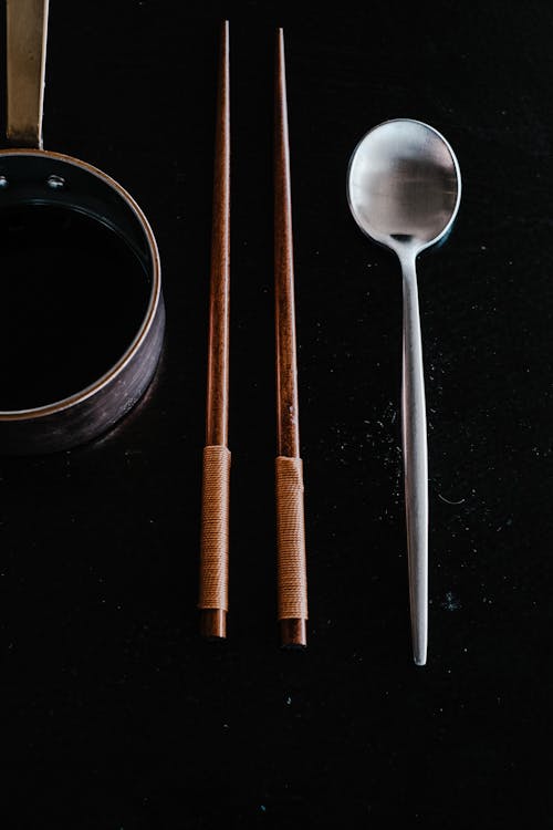 Close-Up Photo of Wooden Chopsticks Beside a Silver Spoon
