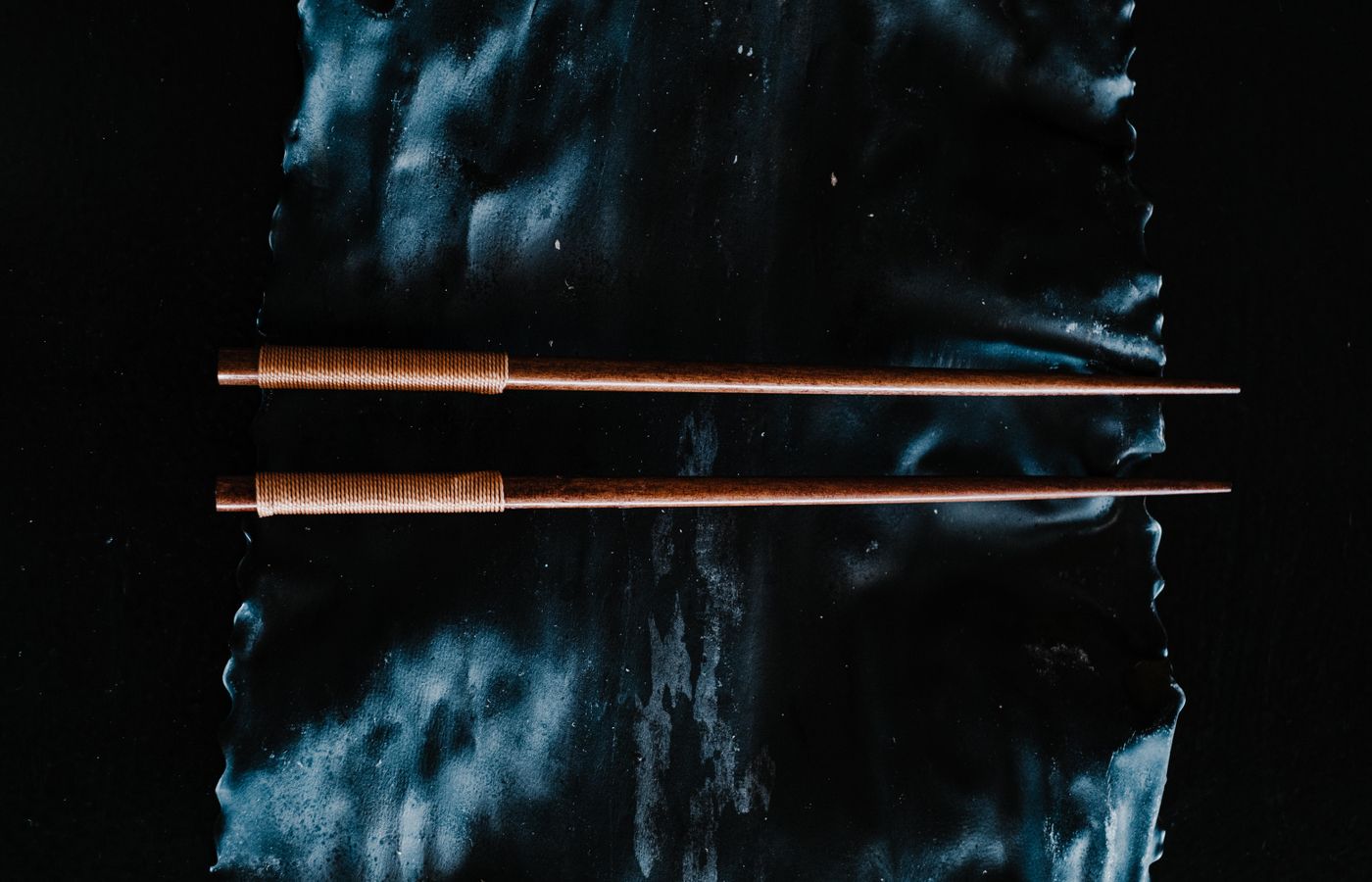 Close-up of wooden chopsticks displayed on a textured dark background, emphasizing minimalist design.