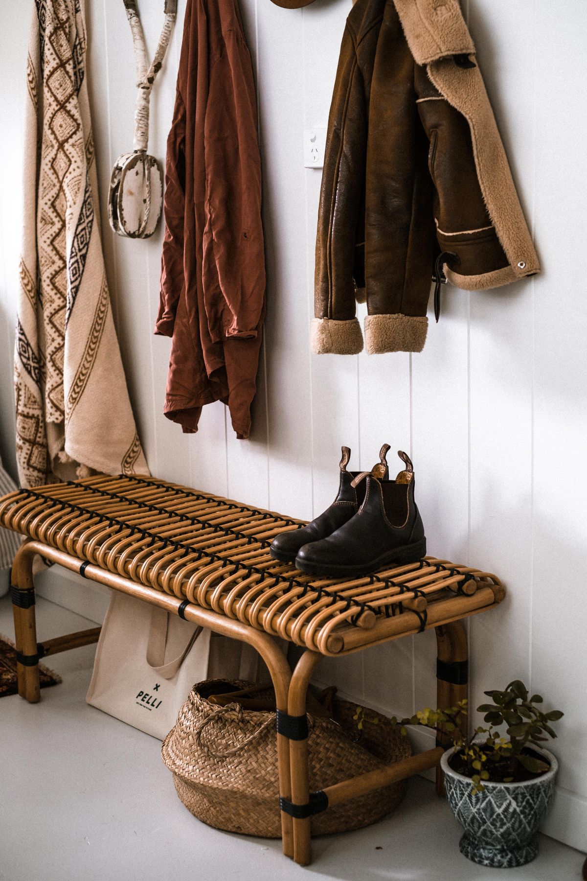 Organized entryway with wall hooks shoes and a woven storage bench