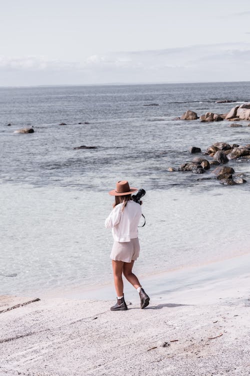 Photo of a Photographer in a White Top Walking at the Beach