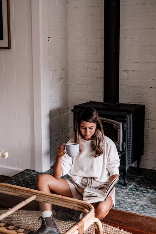 Photo of a Woman Reading a Book while Holding a Cup