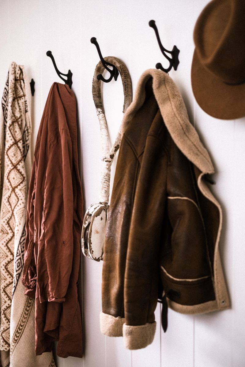 Leather coat and hat hanging on rustic wall hooks in an entryway