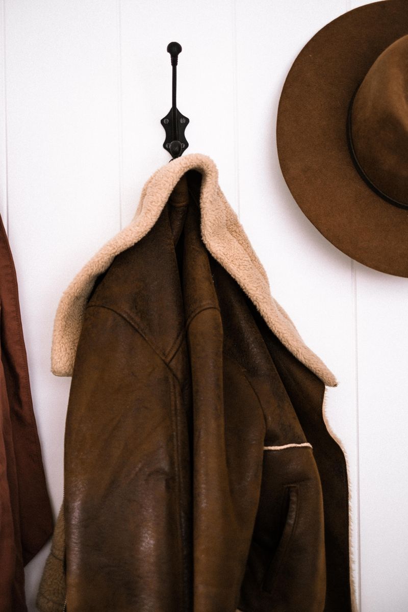 Close-up of a leather jacket and hat hanging on an entryway wall hook