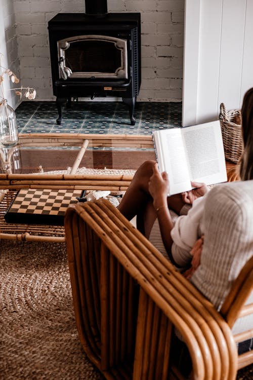 Person Sitting on Brown Bamboo Chair Reading Book