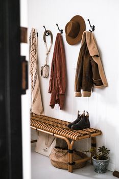 Stylish entryway decor with coats, hat, and boots on rattan bench.