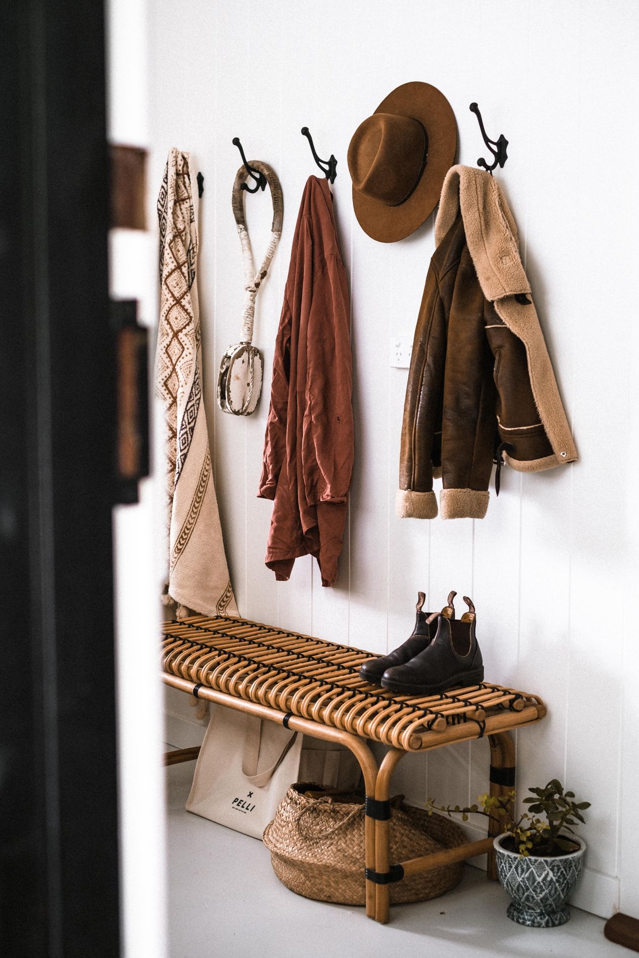 Rattan entryway bench with wall hooks holding coats and hat, baskets below